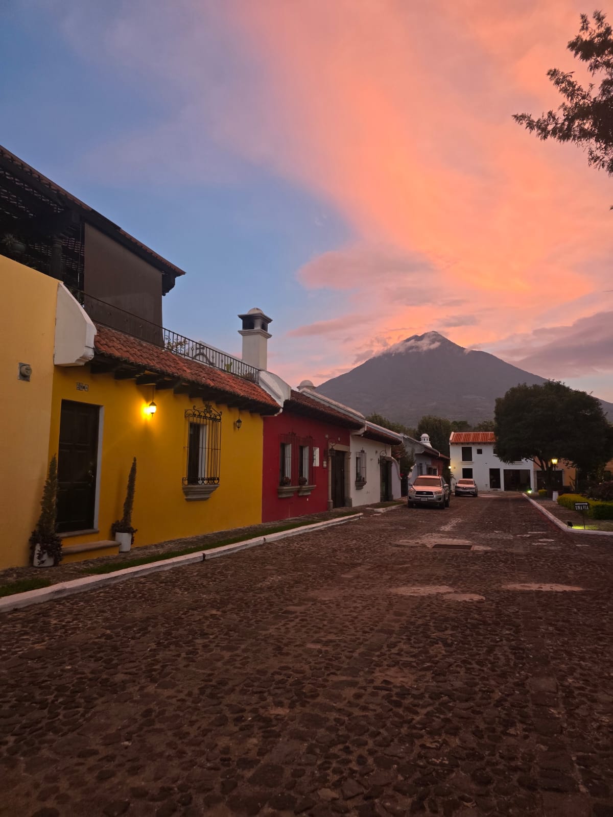 Alrededores de Condesa: casas de colores y una calle empedrada, con un volcán bajo el cielo rosado del atardecer